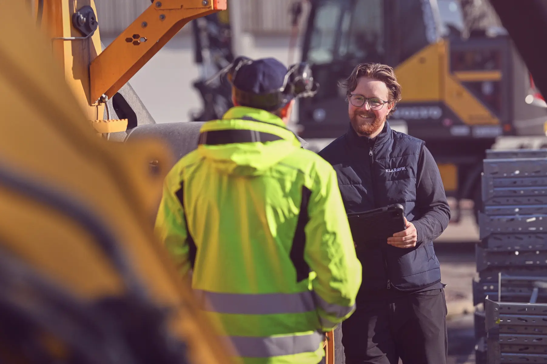 A Klaravik employee with a tablet talking to a customer in front of machinery